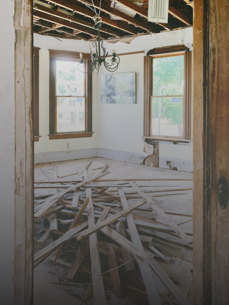 Distressed property interior with exposed ceiling, structural damage, and debris, showing need for stabilization before renovations.