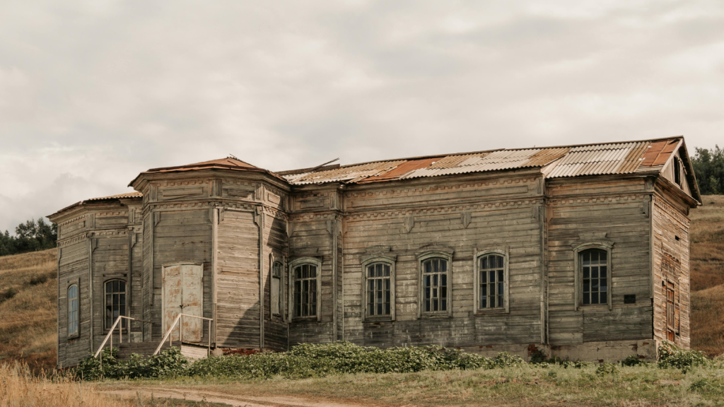 Distressed wooden property with visible roof wear, aging siding, and structural deterioration in a rural setting