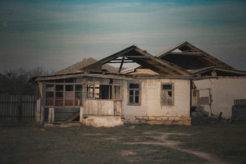 Vacant distressed property with structural damage, deteriorating roof, and visible deferred maintenance
