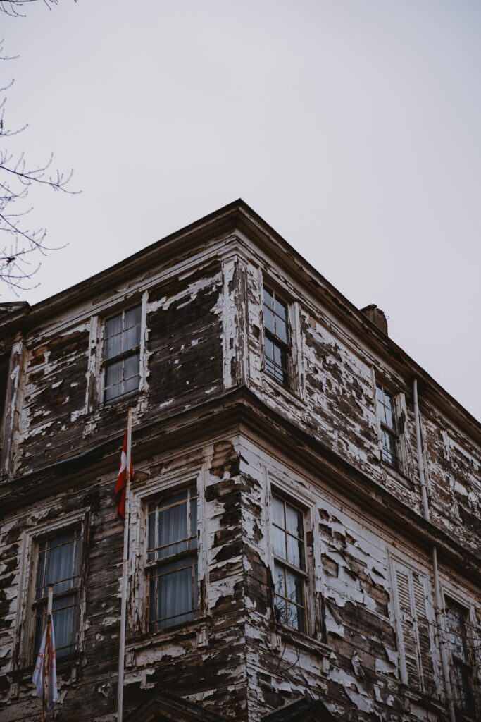 Abandoned multi-story property with peeling paint and visible exterior deterioration caused by long-term neglect and weather exposure.