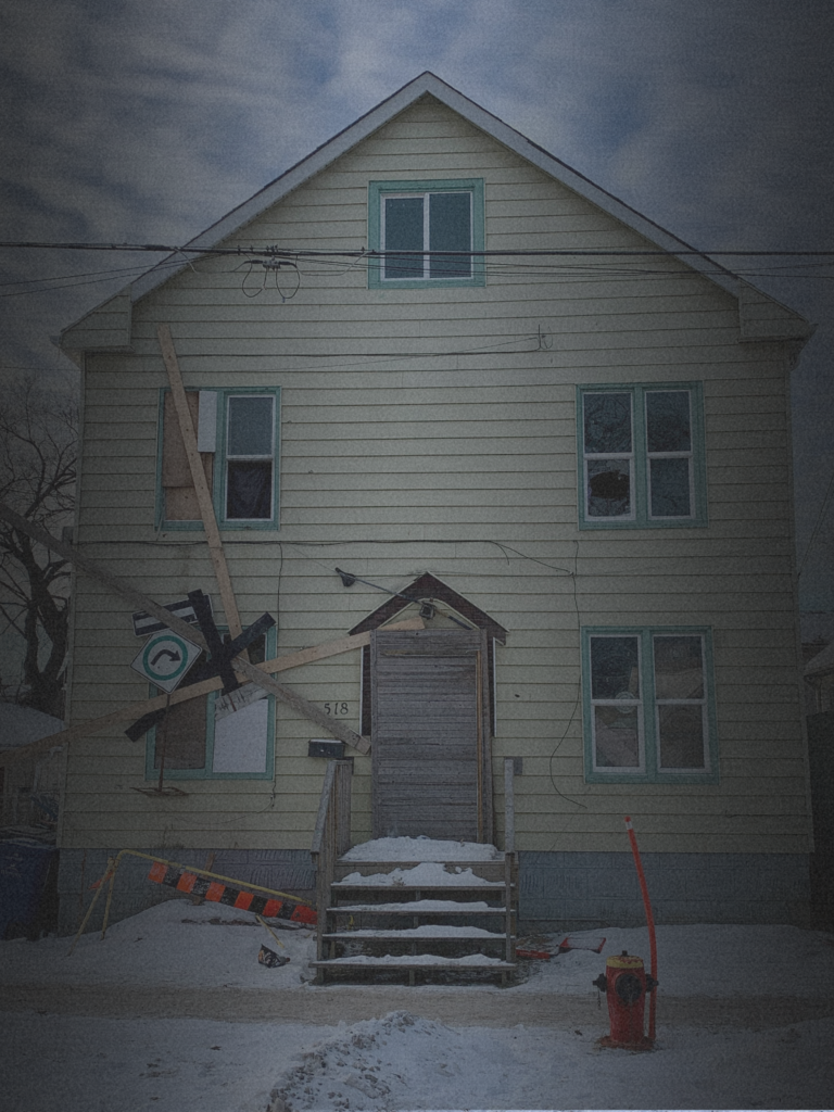 Vacant multi-story house with boarded windows, broken glass, temporary repairs, and snow-covered ground illustrates the operational challenges and risks of real estate investing.