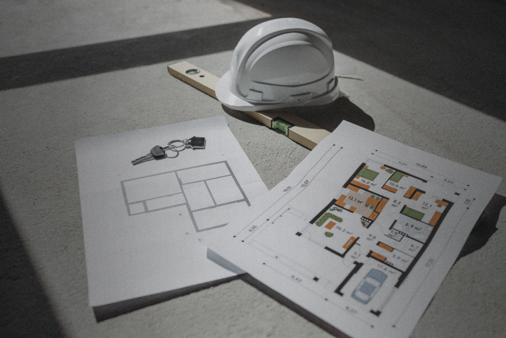 Construction plans, house keys, and a hard hat arranged on a table, symbolizing the discipline and planning required for successful real estate investing.