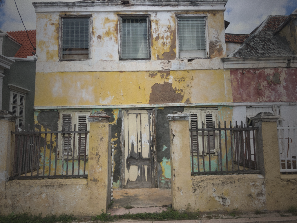 Distressed residential property with peeling paint. weathered exterior walls. deteriorated fencing, and visible signs of deferred maintenance, illustrating the hidden costs and risks of cheap real estate investments.
