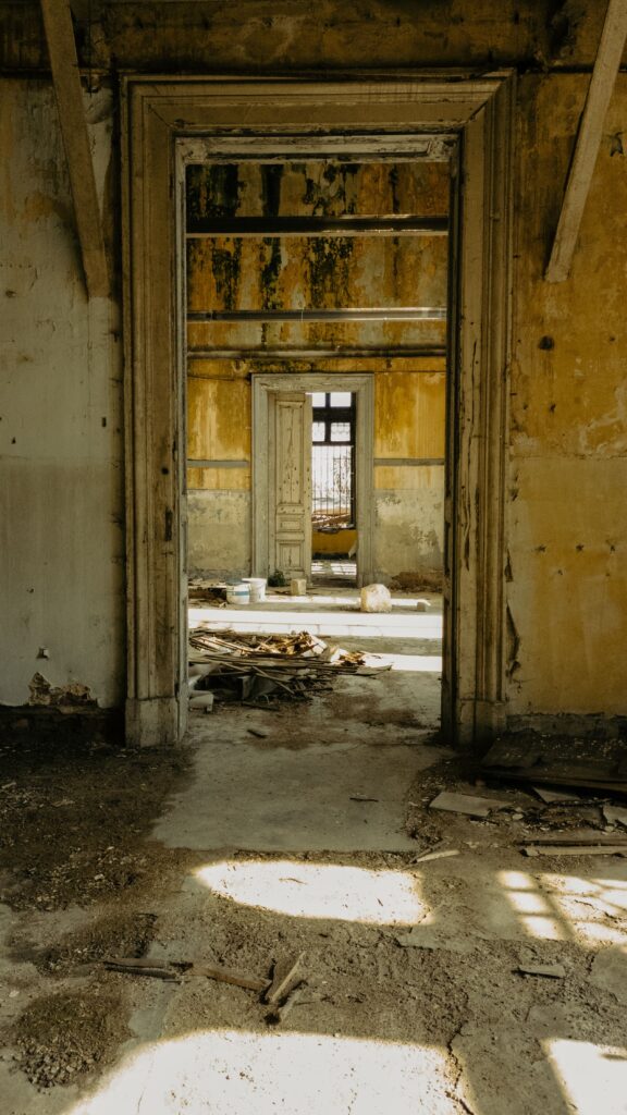 Interior of a distressed vacant property with peeling walls, debris, and multiple doorways before renovation.